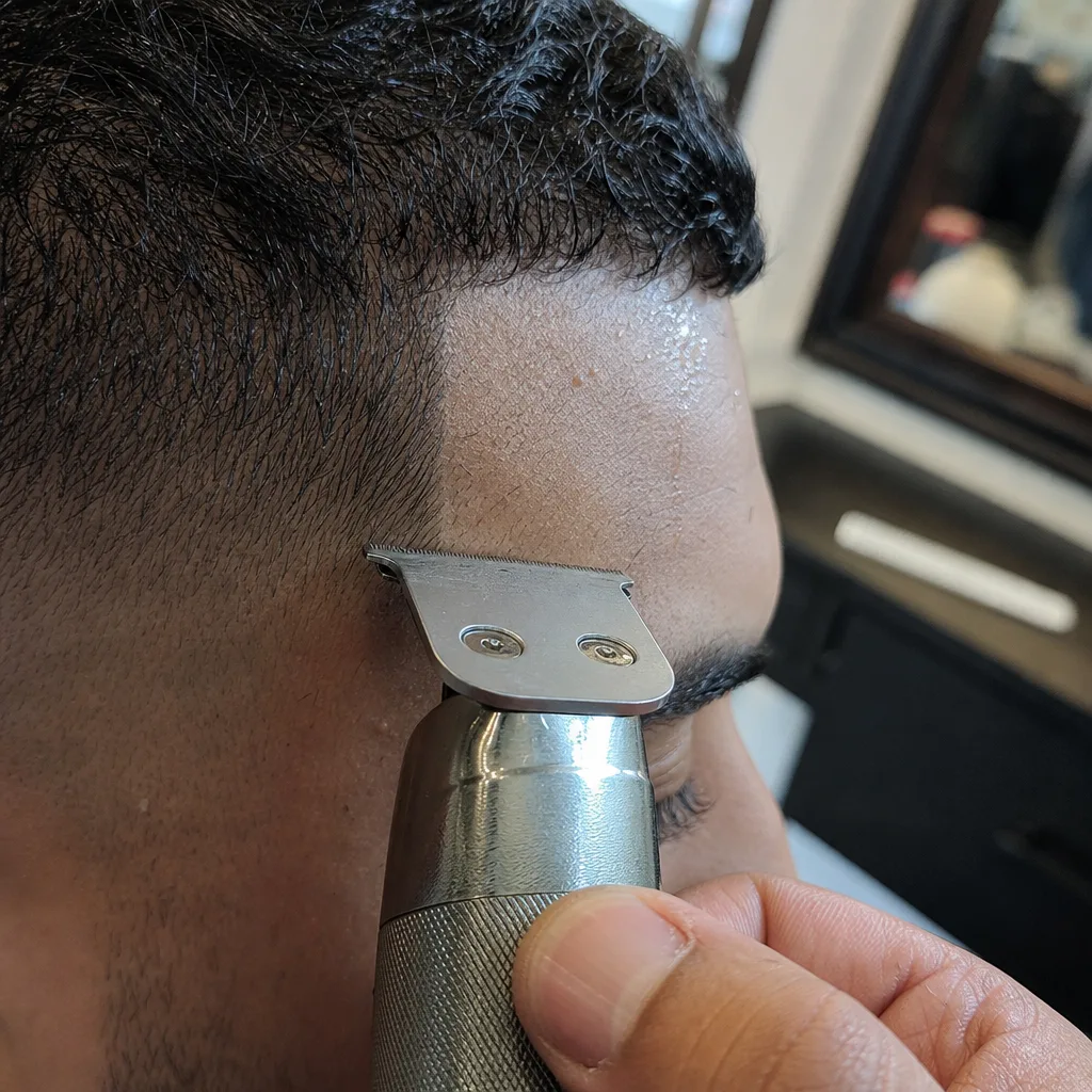 Close-up of trimmer cutting sharp hairline edge during barbershop line up Newark